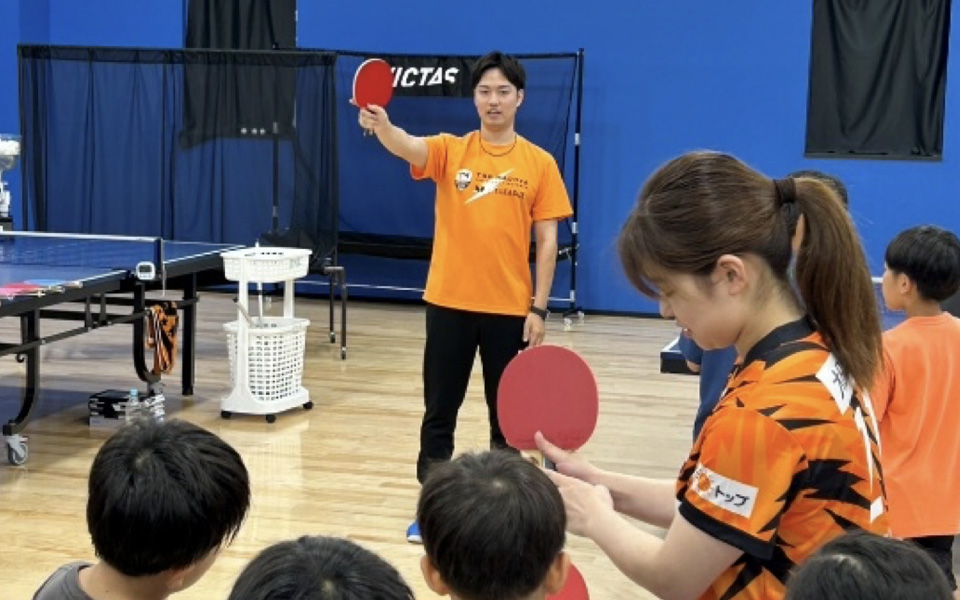 ラケットを持って卓球を教える監督と選手